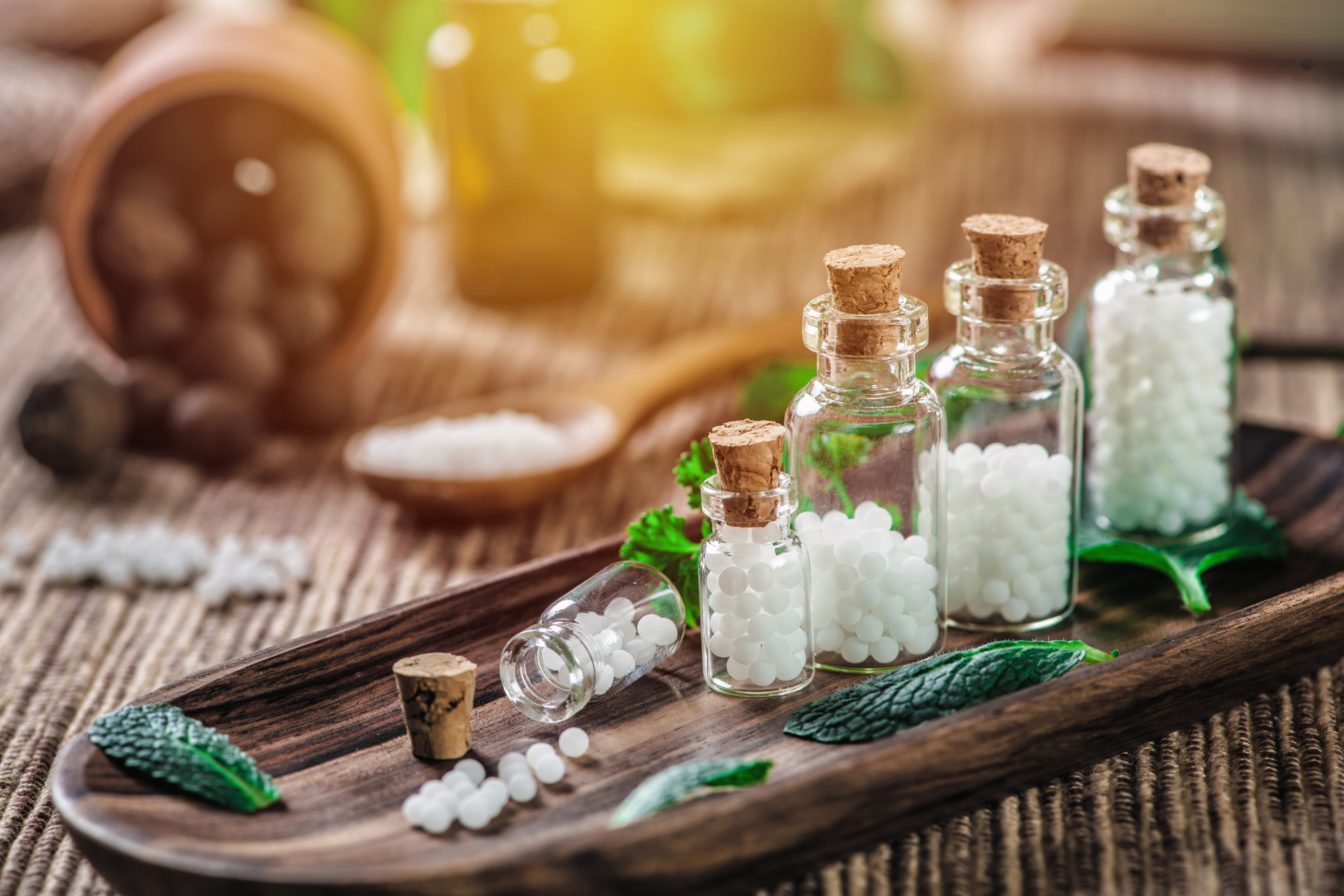 Flaconi di vetro con rimedi omeopatici e foglie di menta su un vassoio di legno.